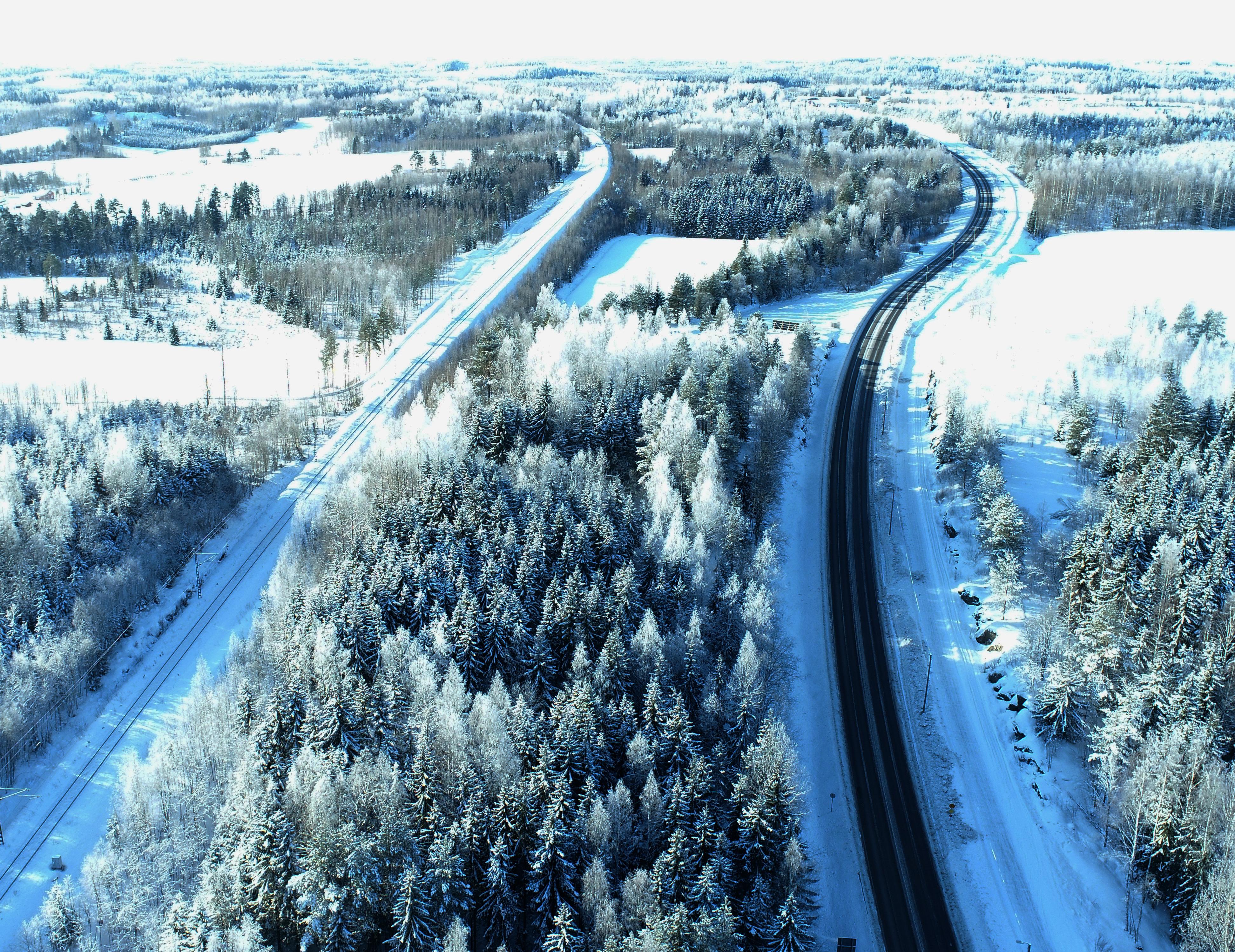 Ylhäältä kuvattu talvinen maisema, puita ja teitä.