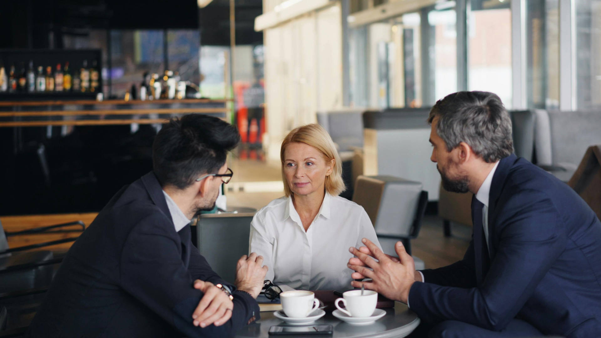 Ihmisiä kahvilassa, kaksi miestä ja nainen.