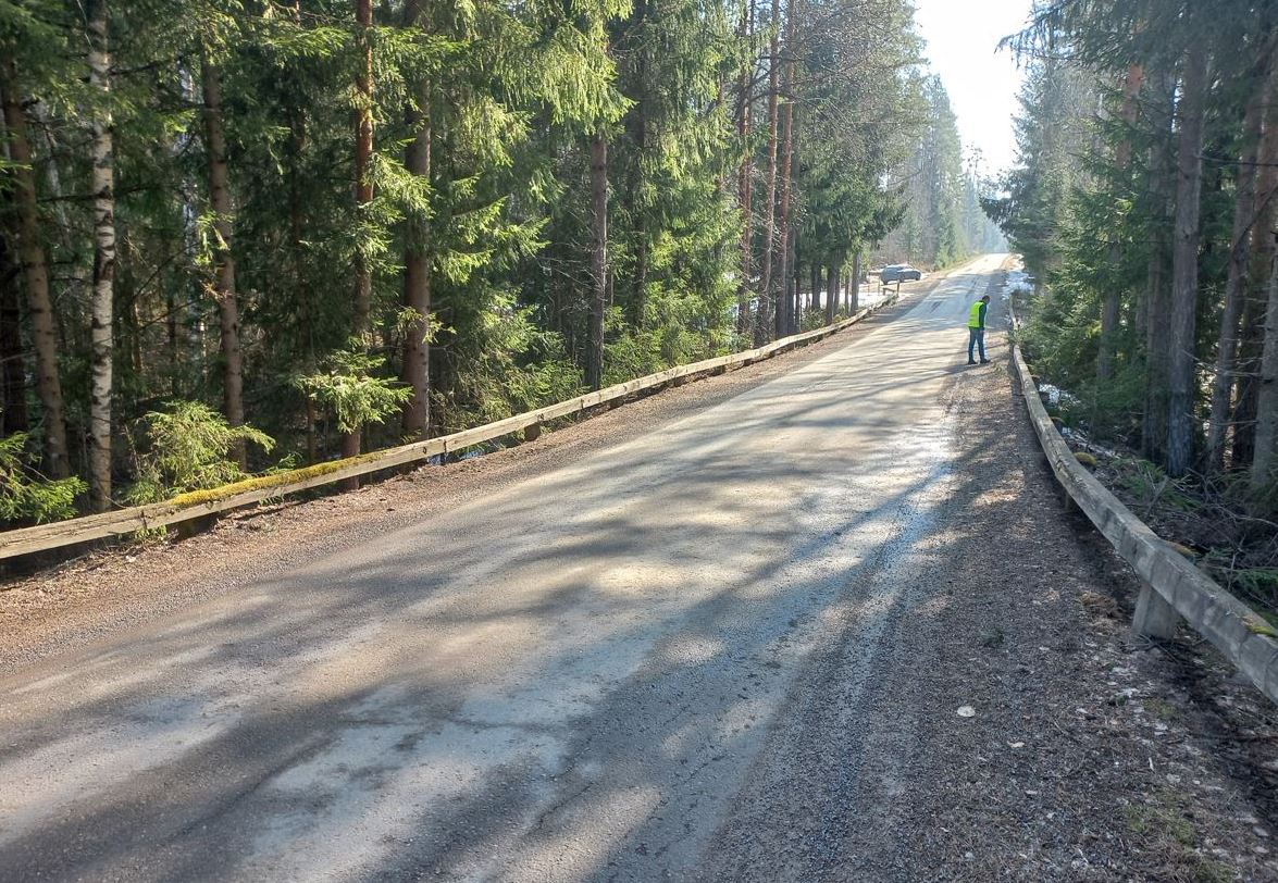 Huomioliivit päällä oleva henkilö tarkastelemassa soratiellä olevaa sillan kantta. 